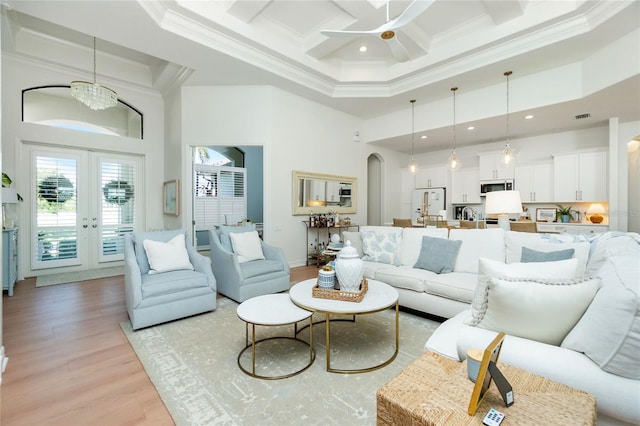 living room featuring light hardwood / wood-style flooring, a high ceiling, french doors, ceiling fan with notable chandelier, and ornamental molding