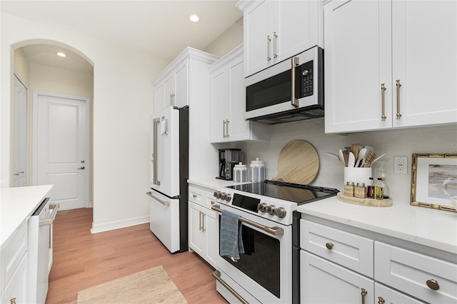 kitchen with white cabinetry, light stone counters, light wood-type flooring, tasteful backsplash, and premium appliances