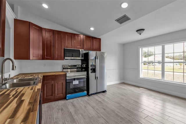 kitchen with vaulted ceiling, butcher block counters, light wood-type flooring, appliances with stainless steel finishes, and sink