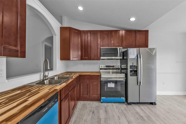 kitchen with vaulted ceiling, appliances with stainless steel finishes, light wood-type flooring, sink, and butcher block counters