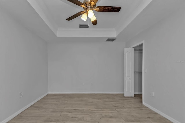 empty room with a raised ceiling, ceiling fan, ornamental molding, and light hardwood / wood-style flooring