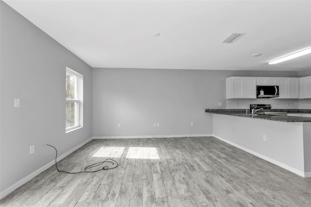 kitchen featuring kitchen peninsula, light wood-type flooring, white cabinets, appliances with stainless steel finishes, and dark stone countertops