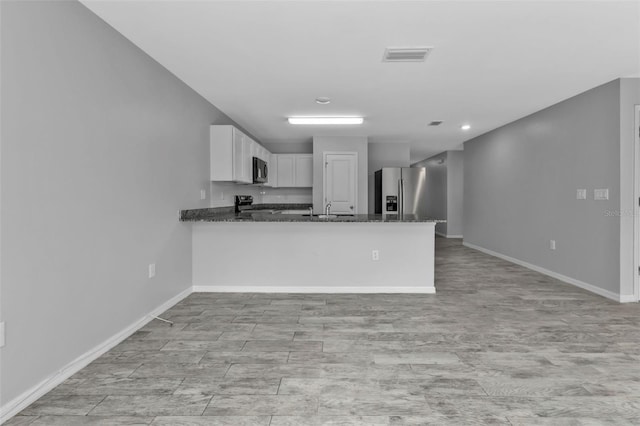 kitchen featuring stainless steel fridge, white cabinetry, dark stone counters, and kitchen peninsula