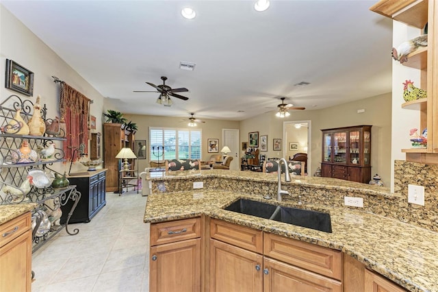 kitchen with kitchen peninsula, ceiling fan, light tile patterned flooring, light stone counters, and sink