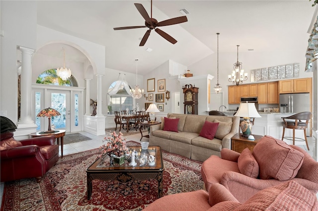 tiled living room with high vaulted ceiling, decorative columns, and ceiling fan with notable chandelier