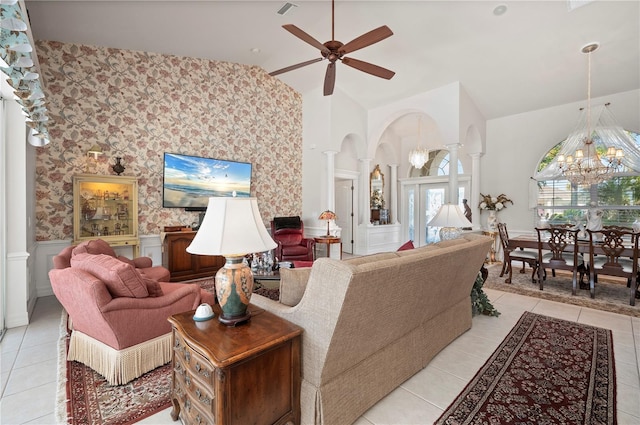 tiled living room with lofted ceiling, ceiling fan with notable chandelier, and ornate columns