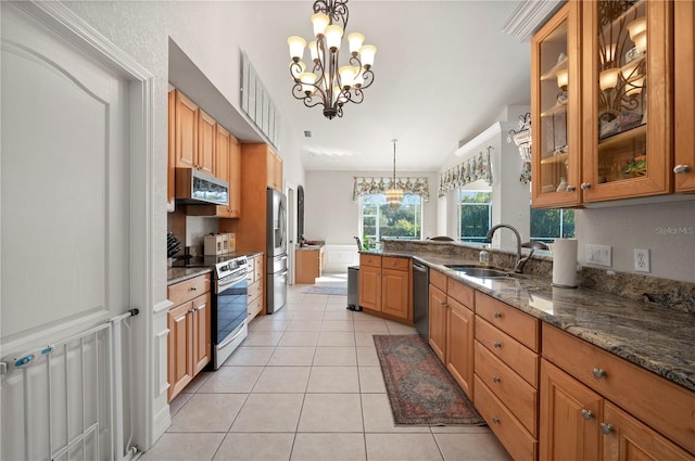 kitchen featuring decorative light fixtures, light tile patterned floors, appliances with stainless steel finishes, dark stone countertops, and sink