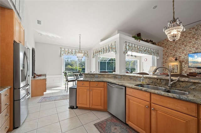 kitchen with hanging light fixtures, stainless steel appliances, light tile patterned floors, dark stone countertops, and sink