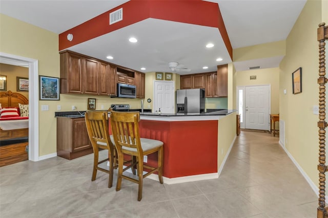 kitchen with kitchen peninsula, stainless steel appliances, light tile patterned floors, a breakfast bar, and ceiling fan