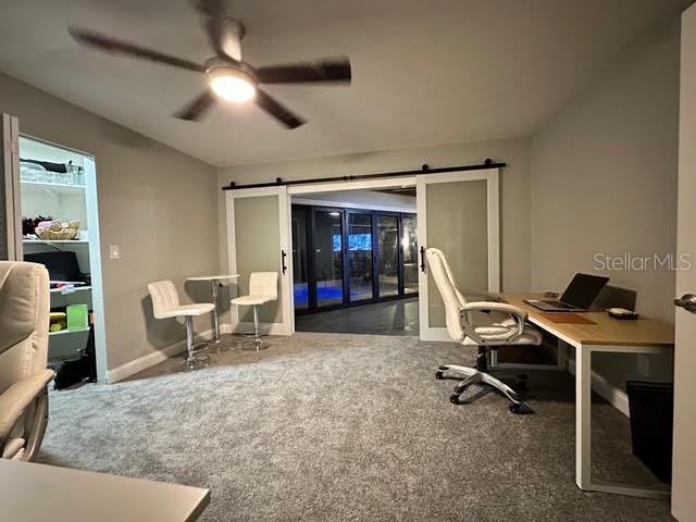 office area with ceiling fan, a barn door, and dark colored carpet