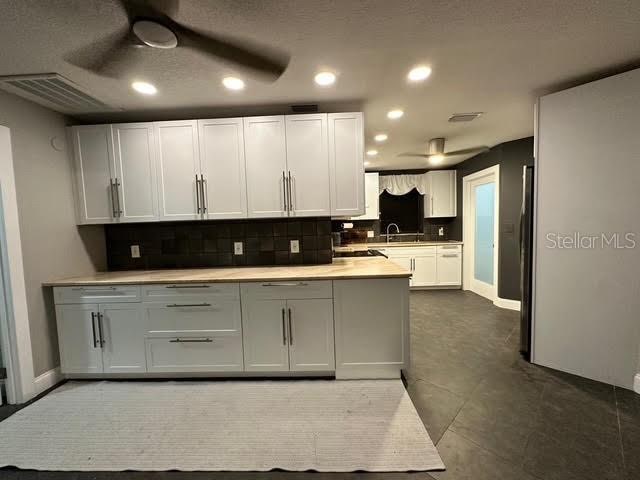 kitchen featuring sink, white cabinets, ceiling fan, tasteful backsplash, and dark tile patterned floors