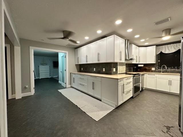 kitchen featuring white cabinetry, ceiling fan, decorative backsplash, wall chimney range hood, and double oven range