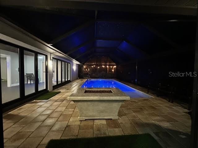 pool at night featuring a lanai, a patio area, and a hot tub