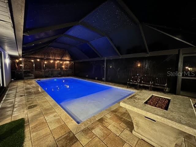 pool at twilight featuring an outdoor fire pit, a patio, and glass enclosure