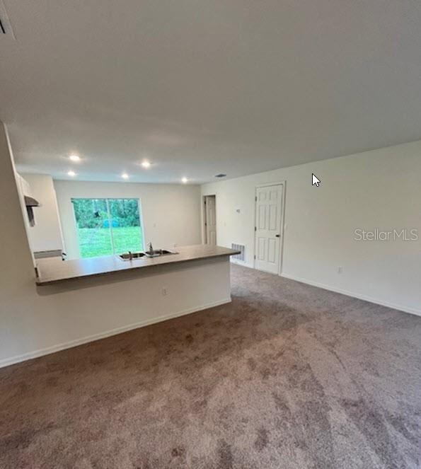 carpeted empty room with recessed lighting, visible vents, a sink, and baseboards