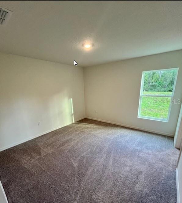 carpeted spare room featuring visible vents, a textured ceiling, and baseboards