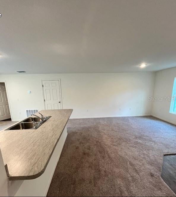 kitchen with baseboards, dark carpet, open floor plan, and a sink