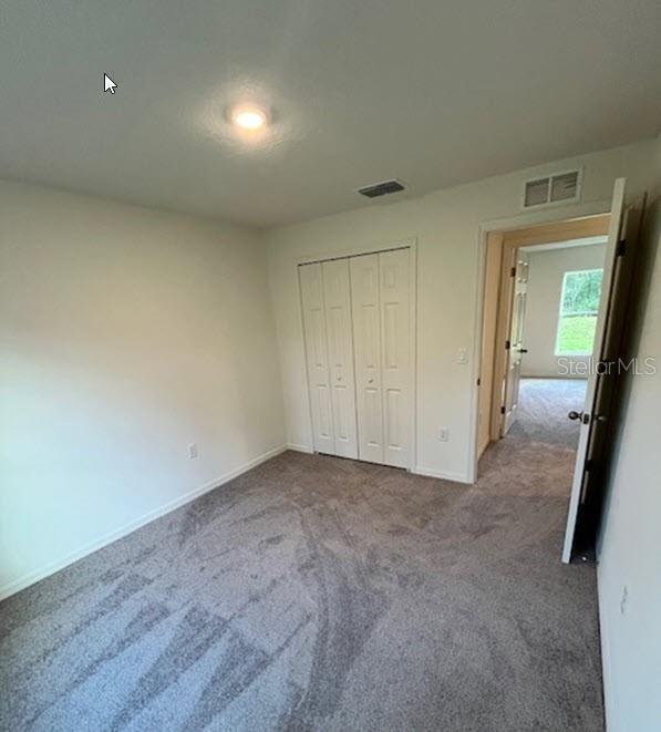 unfurnished bedroom featuring carpet, a closet, visible vents, and baseboards