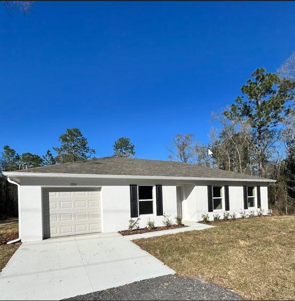 ranch-style house with a garage, concrete driveway, a front lawn, and stucco siding