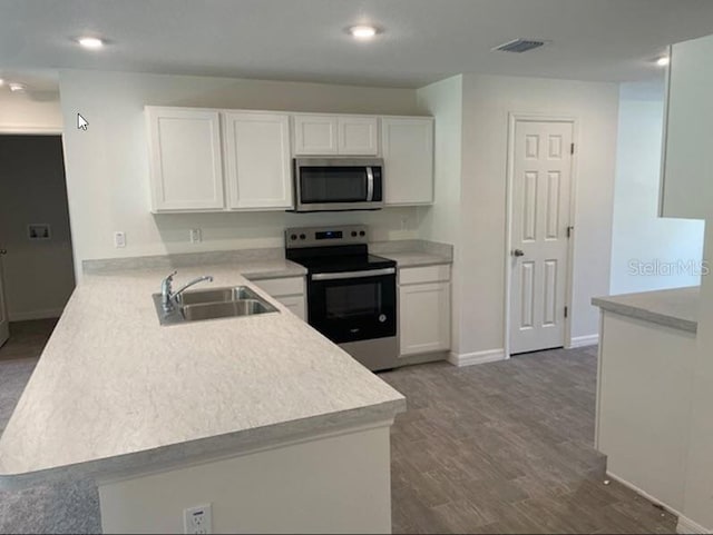 kitchen with appliances with stainless steel finishes, white cabinetry, sink, dark hardwood / wood-style flooring, and kitchen peninsula