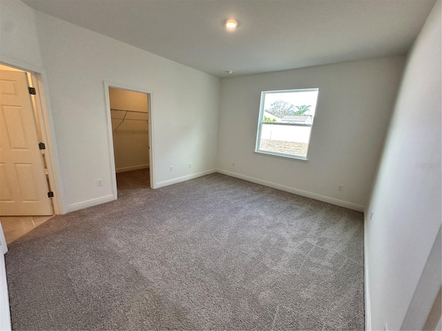 unfurnished bedroom featuring carpet floors, a spacious closet, baseboards, and a closet