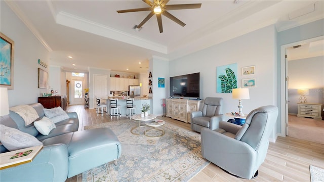 living room with a raised ceiling, ceiling fan, crown molding, and light hardwood / wood-style floors