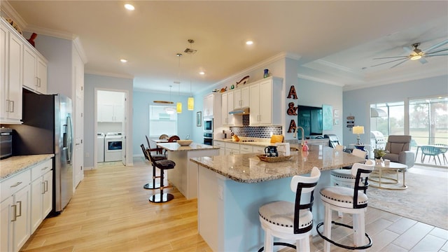 kitchen featuring decorative light fixtures, white cabinets, a kitchen bar, light stone countertops, and a center island with sink