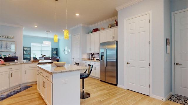 kitchen with light stone countertops, decorative light fixtures, stainless steel refrigerator with ice dispenser, a kitchen island, and white cabinets