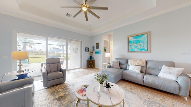 living room with ceiling fan, a tray ceiling, crown molding, and light hardwood / wood-style floors