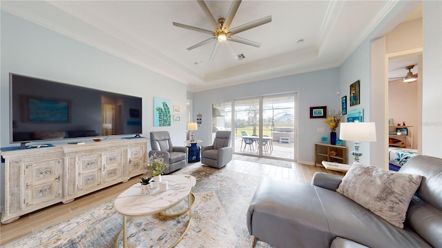 living room with french doors, light wood-type flooring, ceiling fan, a tray ceiling, and ornamental molding