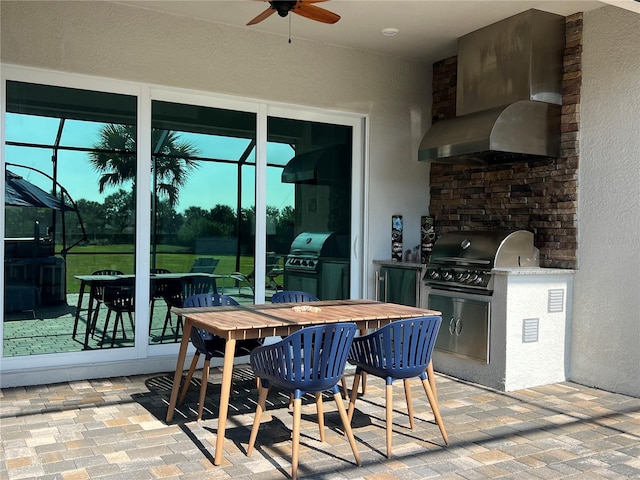 view of patio featuring ceiling fan, glass enclosure, a grill, and an outdoor kitchen