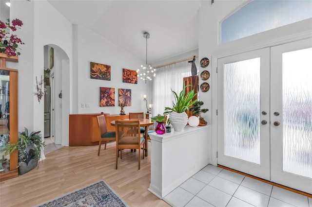 foyer entrance featuring vaulted ceiling, french doors, a chandelier, and light wood-type flooring