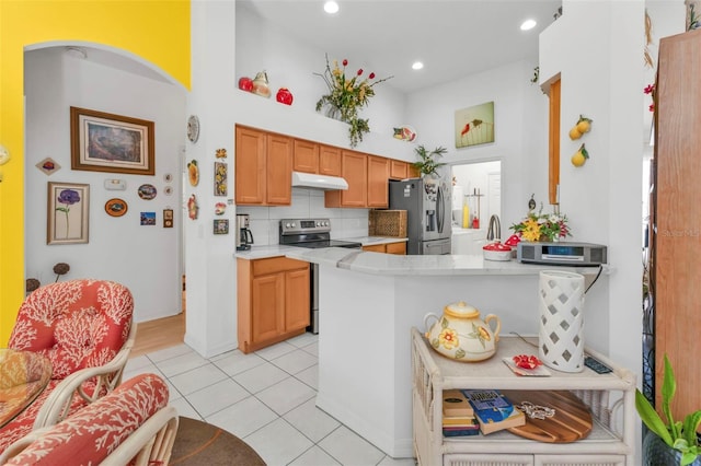 kitchen featuring light tile patterned flooring, a towering ceiling, backsplash, kitchen peninsula, and stainless steel appliances