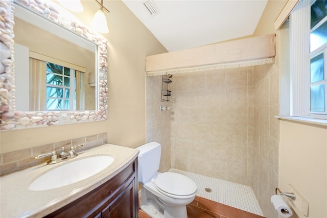 bathroom featuring tile patterned flooring, toilet, tiled shower, vanity, and lofted ceiling