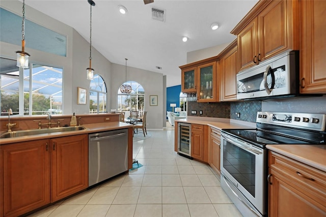 kitchen featuring beverage cooler, appliances with stainless steel finishes, lofted ceiling, decorative light fixtures, and sink