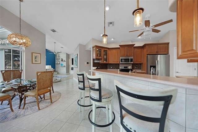 kitchen featuring decorative light fixtures, vaulted ceiling, backsplash, stainless steel appliances, and light tile patterned floors