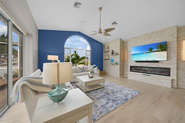 living room featuring light wood-type flooring, ceiling fan, vaulted ceiling, and a stone fireplace