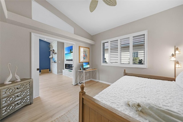 bedroom featuring ceiling fan, vaulted ceiling, a large fireplace, and wood-type flooring