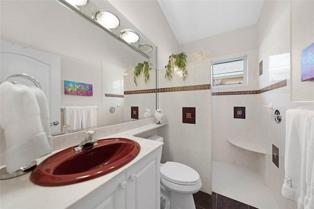 bathroom with tile patterned flooring, vanity, tile walls, toilet, and tiled shower