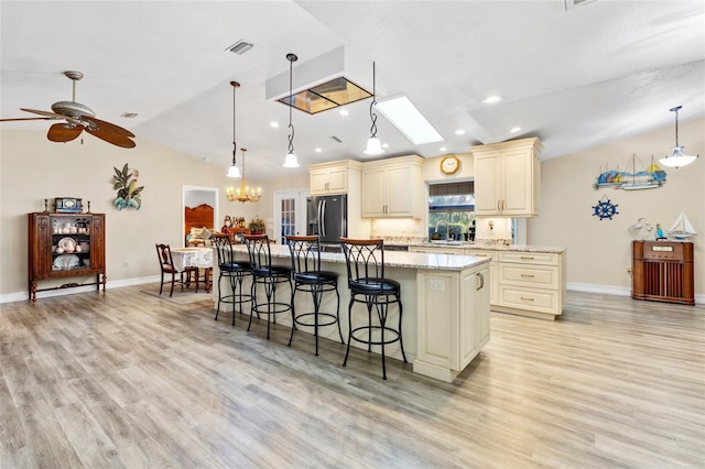 kitchen with vaulted ceiling with skylight, a breakfast bar area, cream cabinets, a center island, and stainless steel fridge