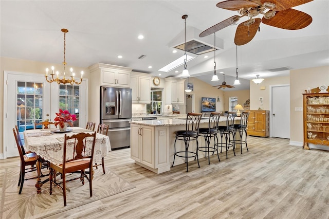 kitchen with light wood finished floors, lofted ceiling, a large island, a kitchen breakfast bar, and stainless steel refrigerator with ice dispenser