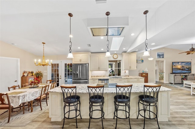 kitchen with stainless steel appliances, a spacious island, vaulted ceiling, and cream cabinets