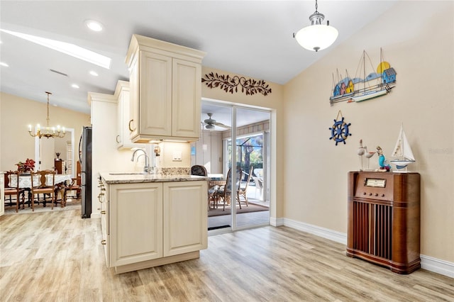 kitchen featuring hanging light fixtures, cream cabinets, stainless steel refrigerator, and light stone counters