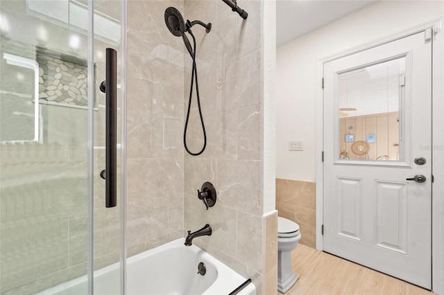 bathroom with enclosed tub / shower combo, toilet, a wainscoted wall, wood finished floors, and tile walls