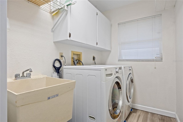 laundry room featuring light wood finished floors, cabinet space, a sink, washer and dryer, and baseboards