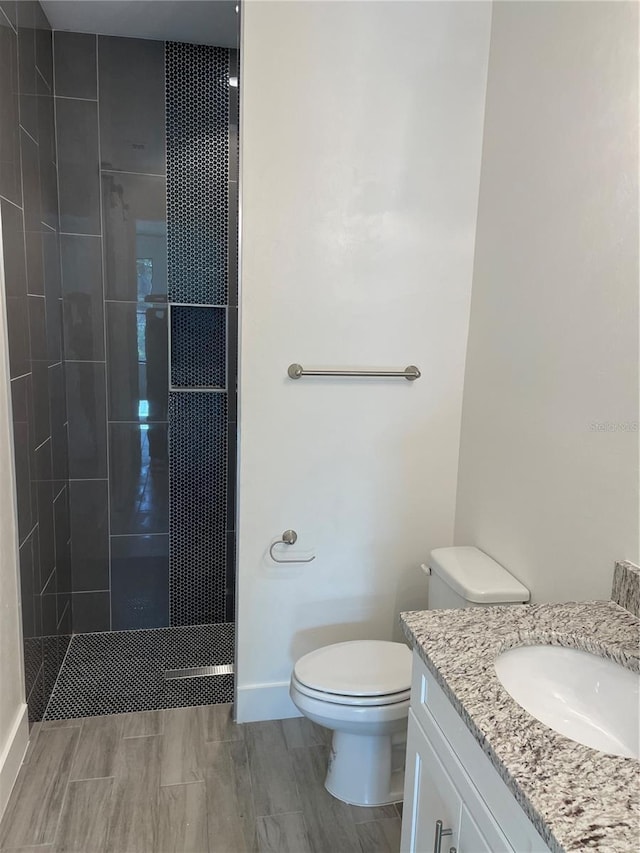 bathroom featuring toilet, a tile shower, and vanity