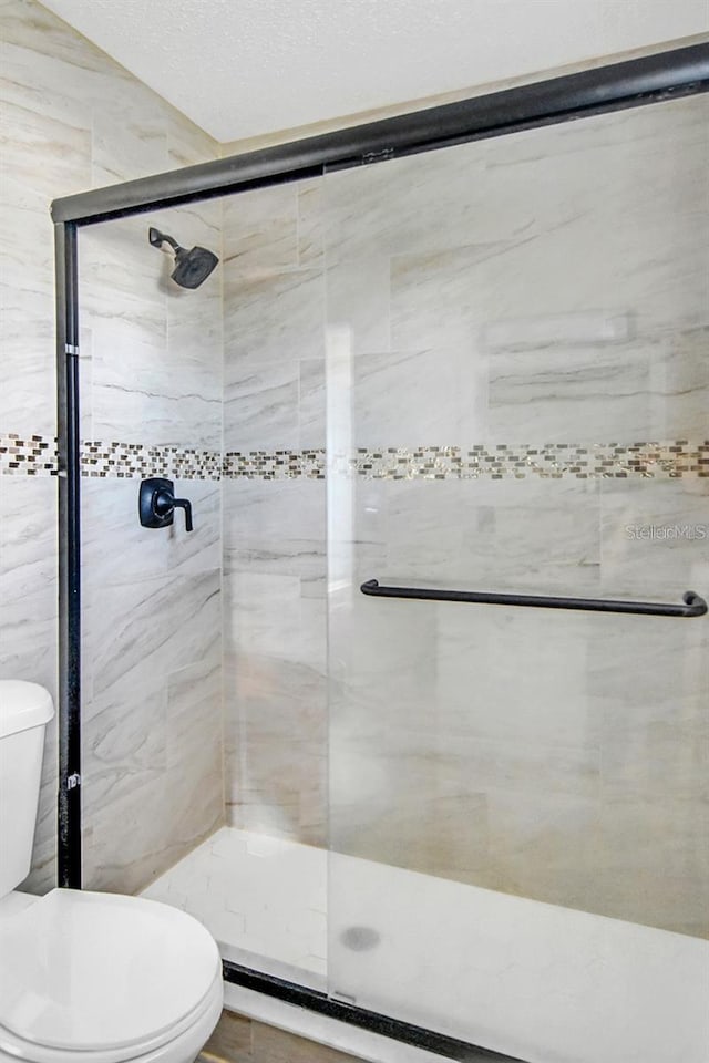 bathroom featuring a shower with shower door and toilet