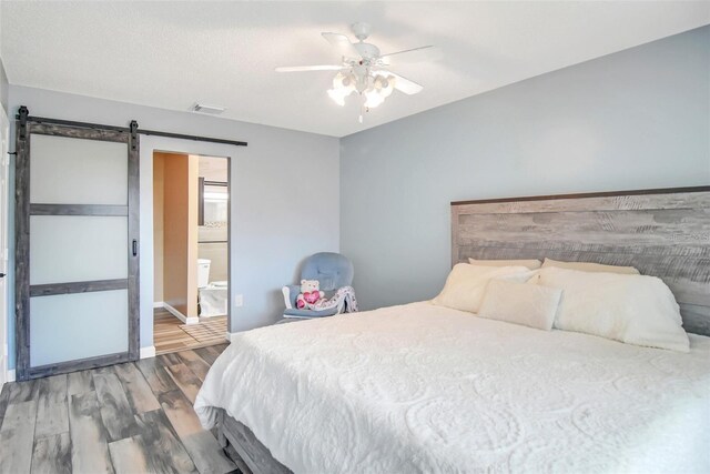 bedroom with a barn door, hardwood / wood-style flooring, ceiling fan, and ensuite bathroom