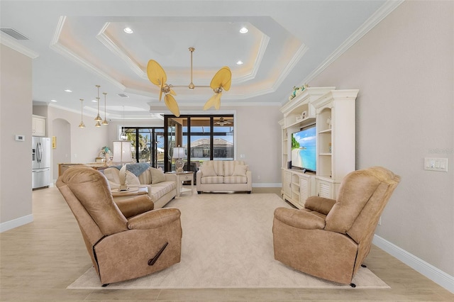 living room with ceiling fan, a tray ceiling, and crown molding