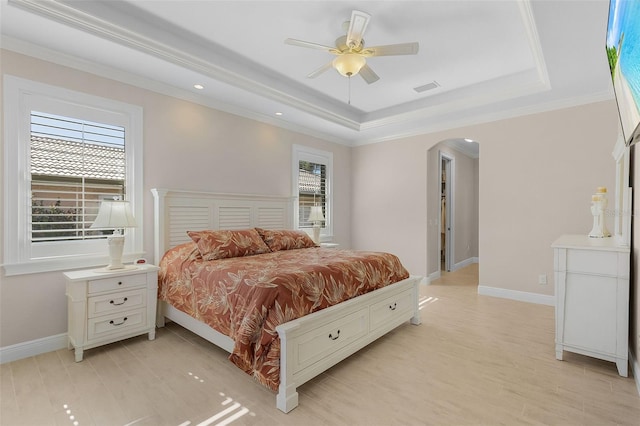 bedroom with ornamental molding, ceiling fan, a tray ceiling, and light hardwood / wood-style floors